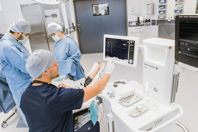 Healthcare professionals in scrubs operate medical equipment in a hospital room.