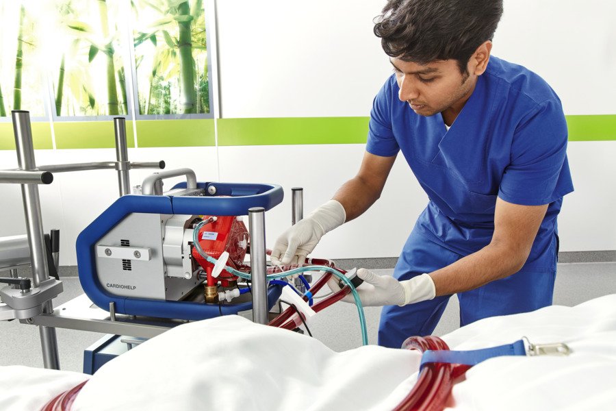 Healthcare professional in blue scrubs adjusting medical equipment beside a patient in a hospital setting.