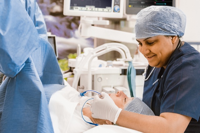 Medical staff attending to a patient in an operating room, wearing surgical attire and caps.