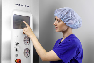 Person in blue scrubs and a hairnet using a touchscreen on a medical device.