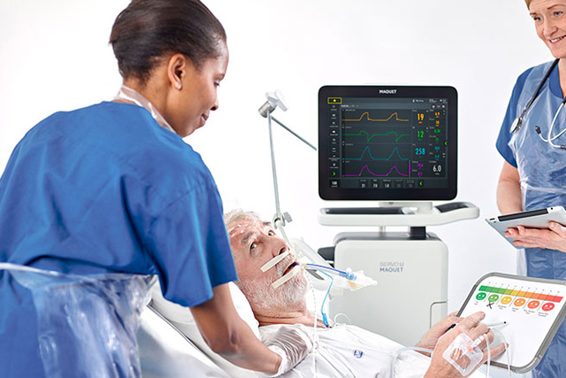 Medical staff monitor a patient in a hospital bed using electronic equipment and tablets.