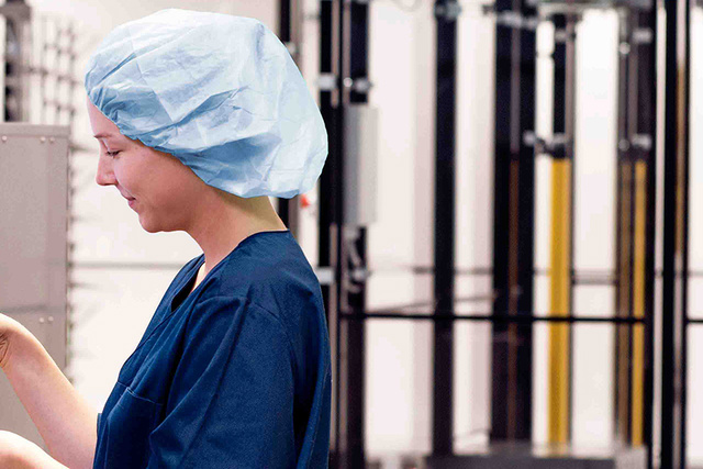 A healthcare worker in scrubs and cap uses a touchscreen near medical equipment.