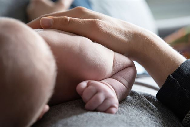 A baby lying on their side with an adults hand gently resting on their back.