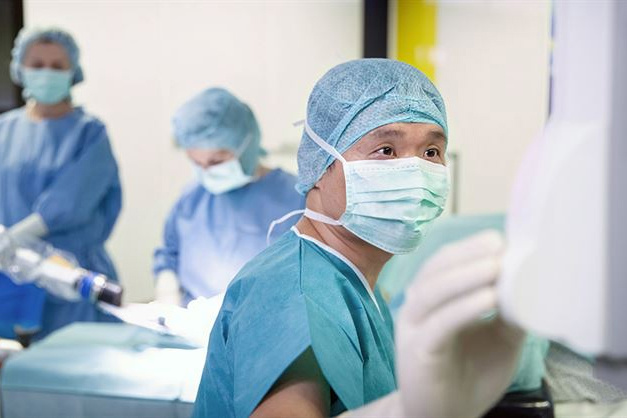 Surgeons in blue scrubs and masks work intently in an operating room, focusing on a medical procedure.