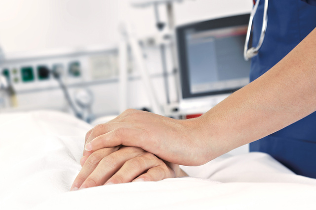 A healthcare professionals hands gently resting on a patients hand in a hospital setting.