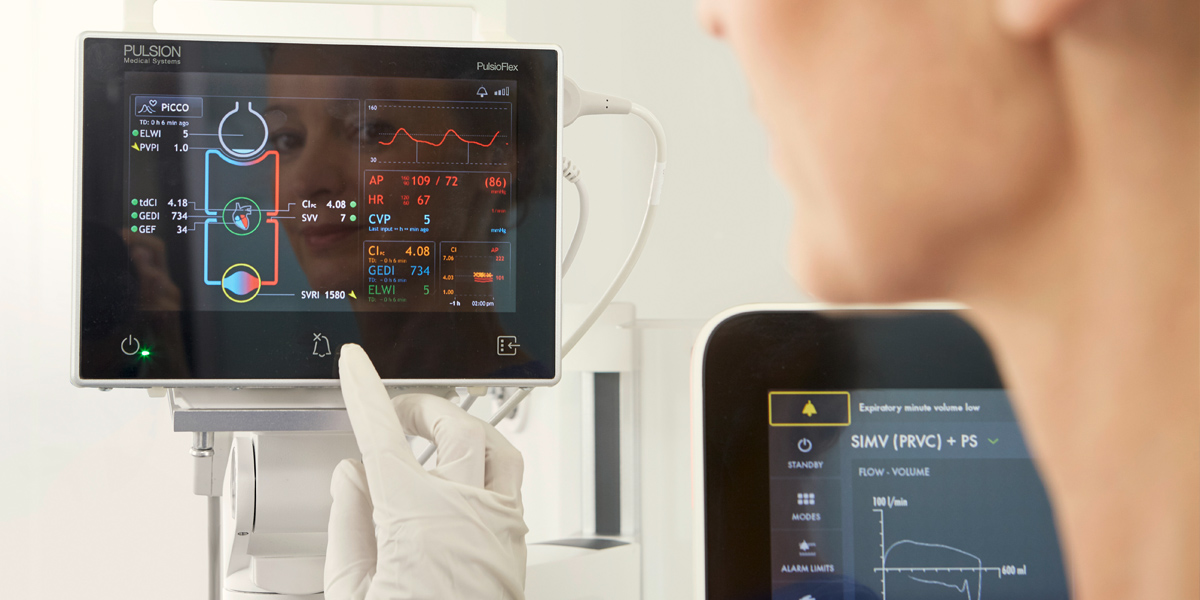 A healthcare professional interacts with a medical monitor displaying patient vital signs and several data graphs.