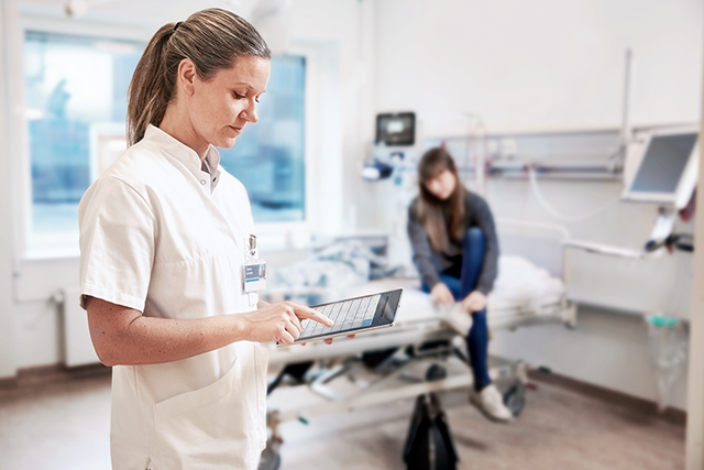 Nurse is updateing the data from a patient on an ipad in a patient room in the hospital