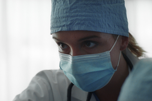 Medical professional wearing a blue surgical cap and mask, focused during a procedure.