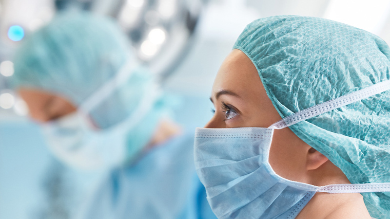 Female surgeon wearing surgical mask and cap, focused during an operation in a brightly lit operating room