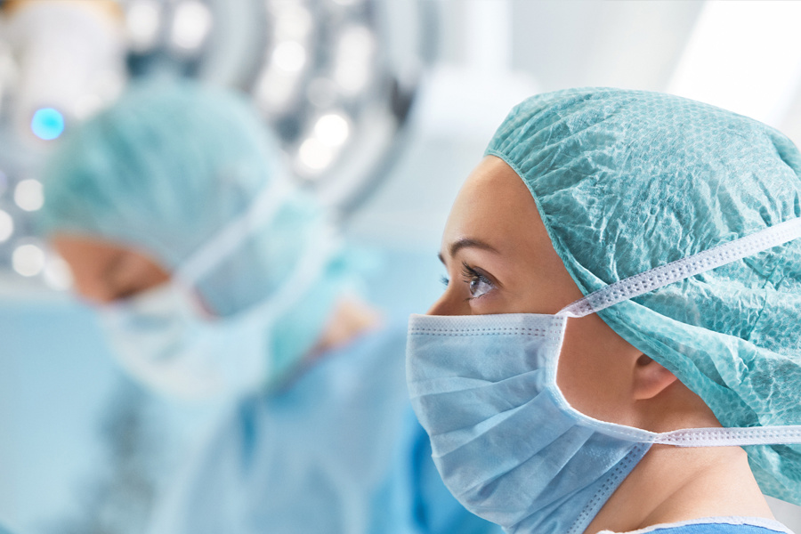 Female surgeon wearing surgical mask and cap, focused during an operation in a brightly lit operating room