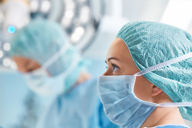 Female surgeon wearing surgical mask and cap, focused during an operation in a brightly lit operating room