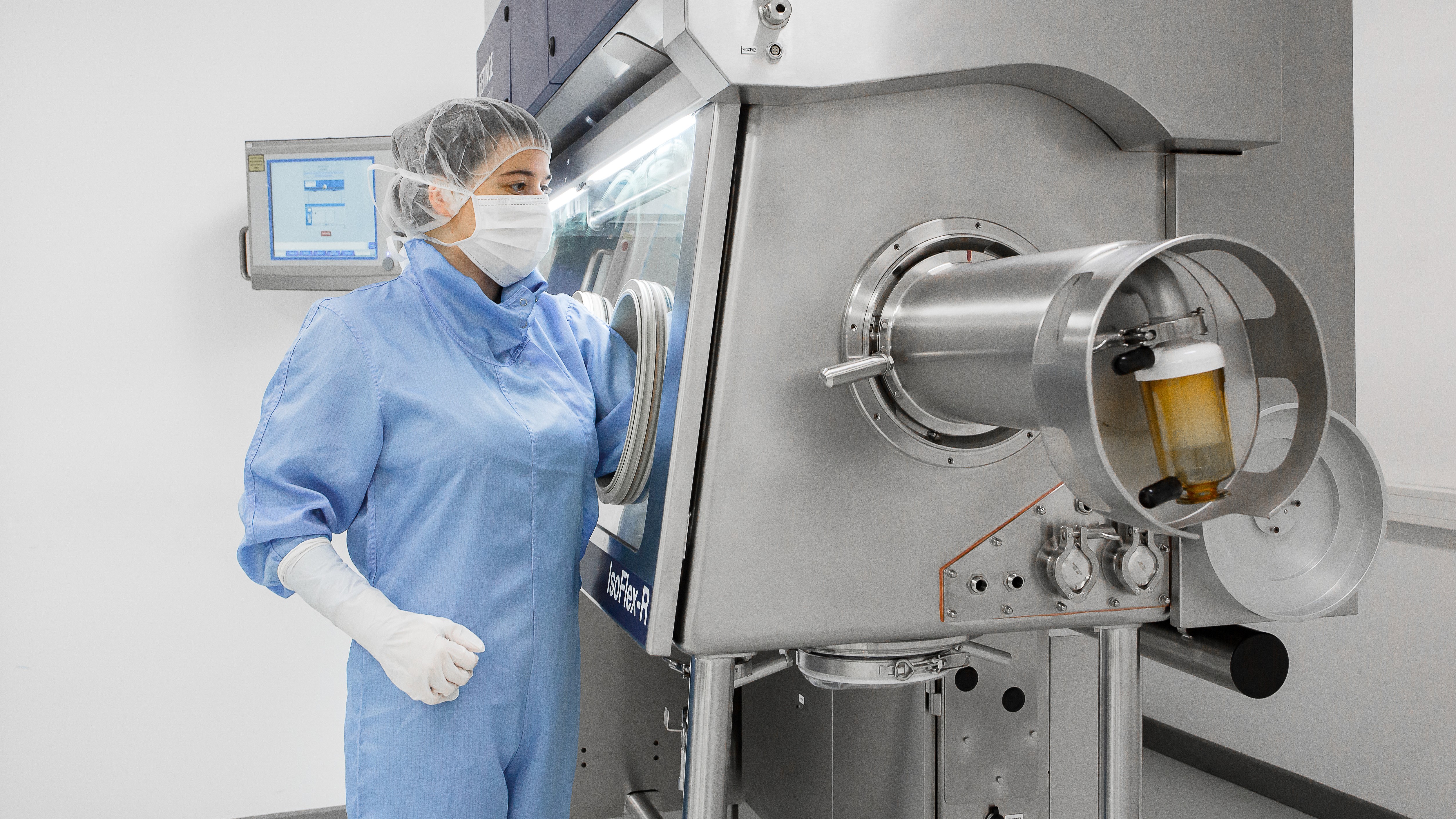 A lab technician in blue protective gear operates a machine in a clean room.