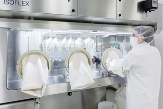 A scientist in protective gear works at an isolator with gloved ports in a laboratory setting.