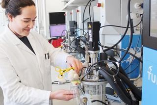 A scientist in a lab coat works with complex laboratory equipment at TU Delft.
