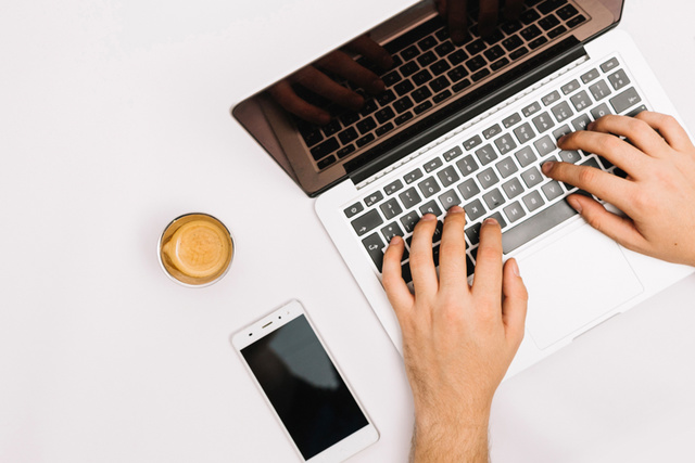 Hands typing on keyboard phone and coffee