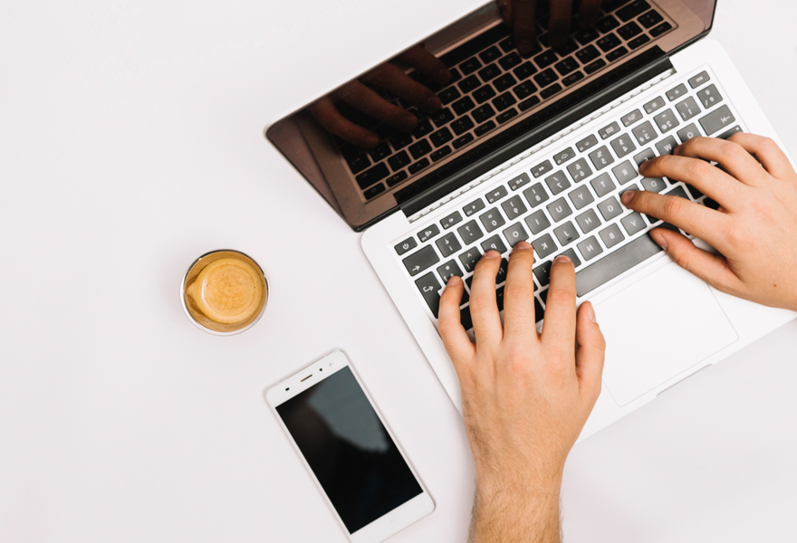 Hands typing on keyboard phone and coffee