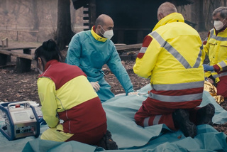 Räddningspersonal i skyddsutrustning tar hand om en person utomhus nära medicinsk utrustning.