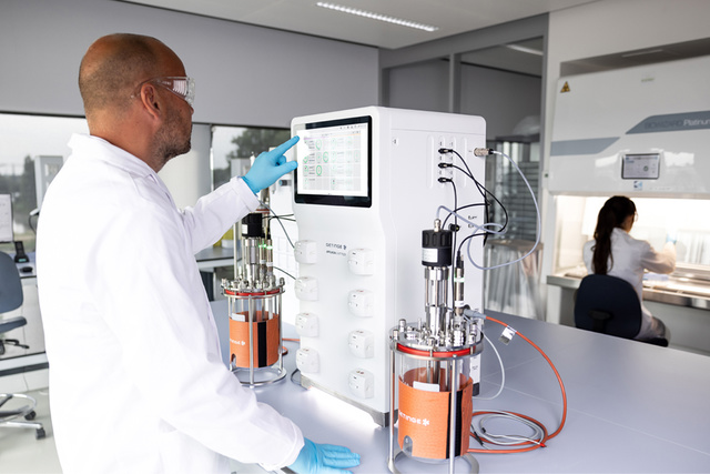 Man in lab coat wearing goggles is working on a display screen