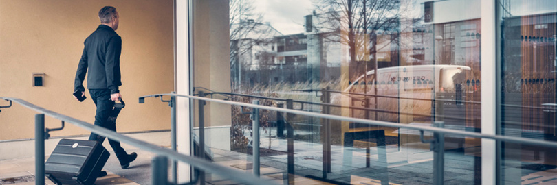 Getinge Servicetechniker betritt mit Rollkoffer ein Klinikgebäude über einen barrierefreien Eingang, um einen Serviceeinsatz durchzuführen.