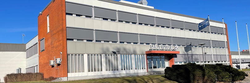 Modernes Industriegebäude mit einer Mischung aus Ziegelstein- und Metallplatten, umgeben von einer Rasenfläche unter einem klaren blauen Himmel.