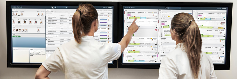 Zwei Personen analysieren Daten auf großen Touchscreens.