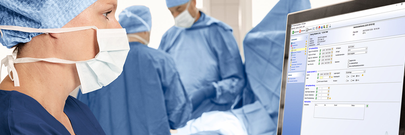 Ein im OP-Kittel und mit Mundschutz gekleideter Mitarbeiter überwacht zusammen mit einem OP-Team in einem Operationssaal Patientendaten auf einem Bildschirm.
