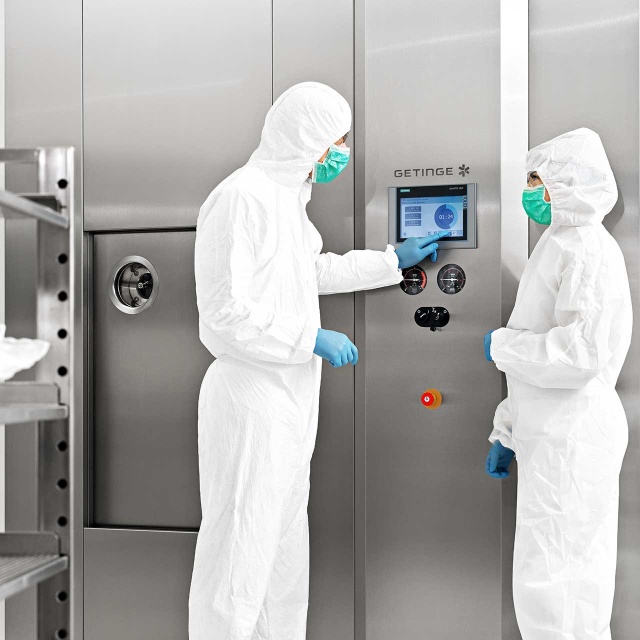 GSS P Steam Sterilizer for pharmaceutical production with a man and a woman working in the front touching the screen for monitoring