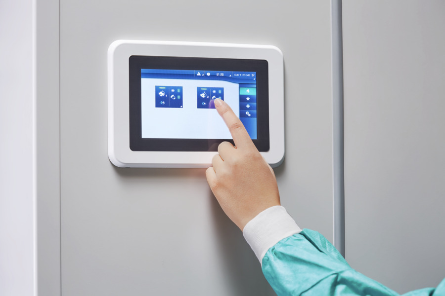 Person in a blue sleeve taps a touchscreen interface on a wall-mounted device.