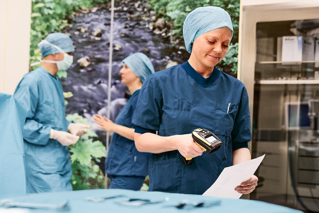 Healthcare professionals in surgical attire working in a hospital, with a nature-themed mural in the background.