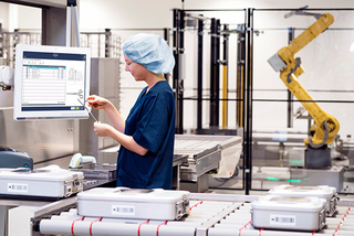 Person in scrubs operates a medical device in a sterile manufacturing environment with robotic machinery.