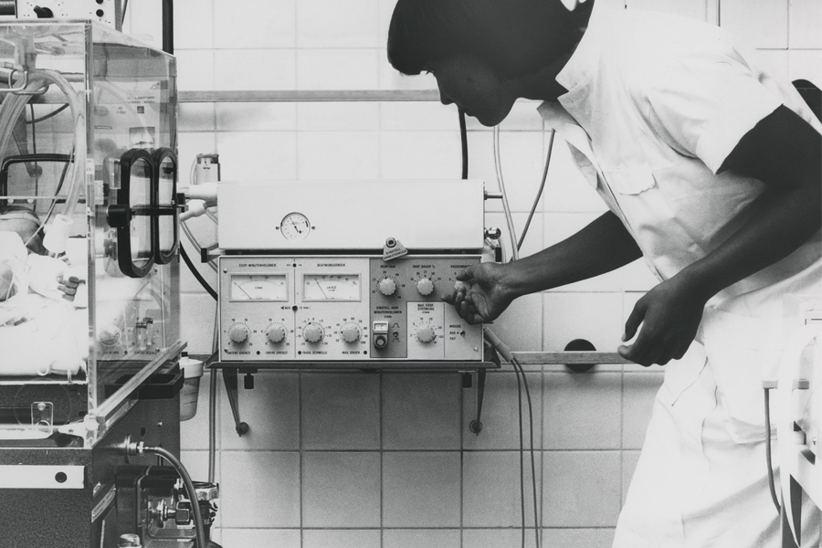 Clinician in nicu ward adjusting Servo 900 ventilator beside neonate in incubator Clinician in nicu ward adjusting Servo 900 ventilator beside neonate in incubator
