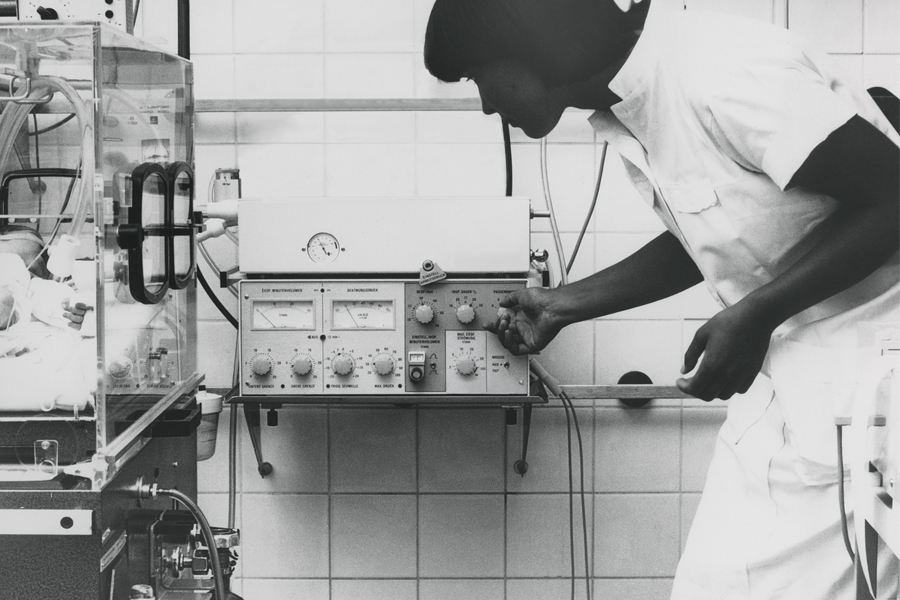 Clinician in nicu ward adjusting Servo 900 ventilator beside neonate in incubator