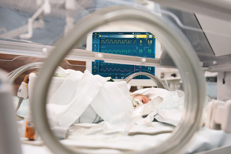 Neonate in incubator with Getinge Servo-n mechanical ventilator screen seen in the background Neonate in incubator with Getinge Servo-n mechanical ventilator screen seen in the background
