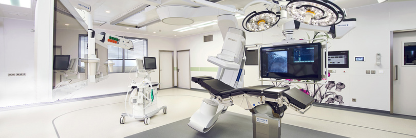 A modern, sterile operating room with surgical equipment and large overhead lights.