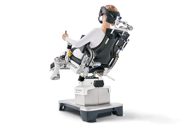 Person using a motion simulator chair with VR headset and controls, mounted on a platform.